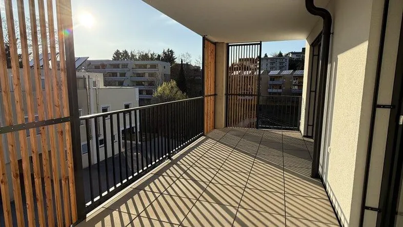 Geräumiger Balkon mit Fliesenboden, Holzlamellen als Sichtschutz und viel Sonnenlicht.