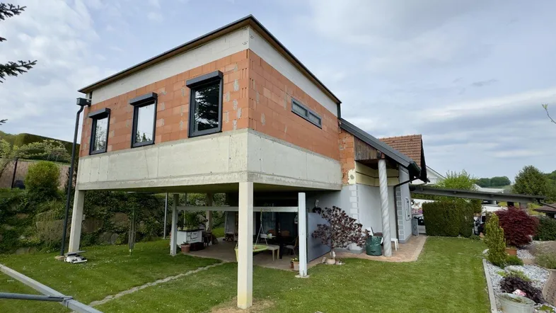 Außenansicht eines Hauses im Bau mit erhöhter Struktur und überdachtem Bereich im Garten.