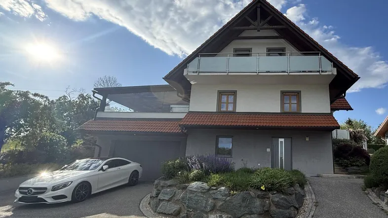 Einfamilienhaus mit Satteldach, Garage und gepflegter Auffahrt unter strahlendem Himmel.