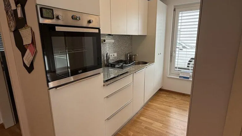 Moderne Einbauküche mit hellen Fronten, Granitarbeitsplatte und integriertem Backofen.