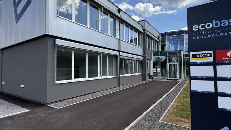 Modernes Bürogebäude mit Glasfassade und Firmenbeschilderung unter blauem Himmel.