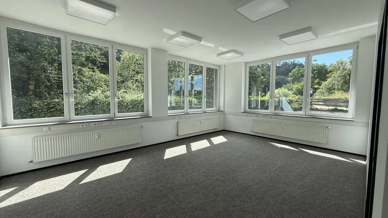 Geräumiges Büro mit großen Fenstern, die viel Tageslicht und einen Blick ins Grüne bieten.