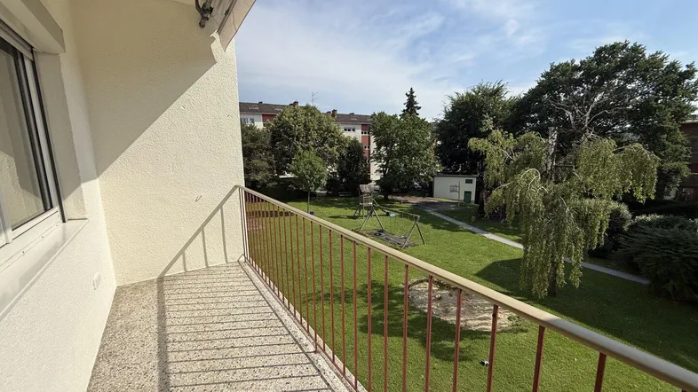 Balkon mit Blick auf den grünen Gemeinschaftsgarten und Kinderspielplatz.