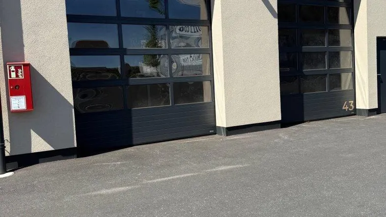 Moderne Gebäudefassade mit zwei großen, verglasten Garagentoren und einer Feuerlöscherbox an der Wand.