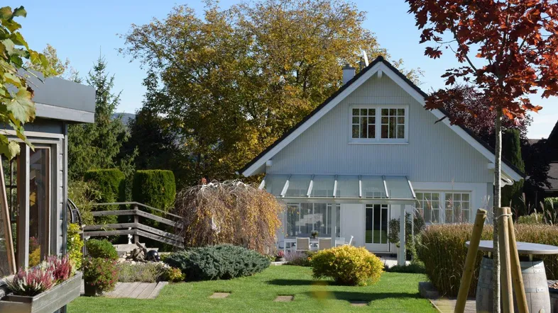 Gepflegter Garten mit Rasenfläche, Bäumen und einem charmanten Haus im Hintergrund.