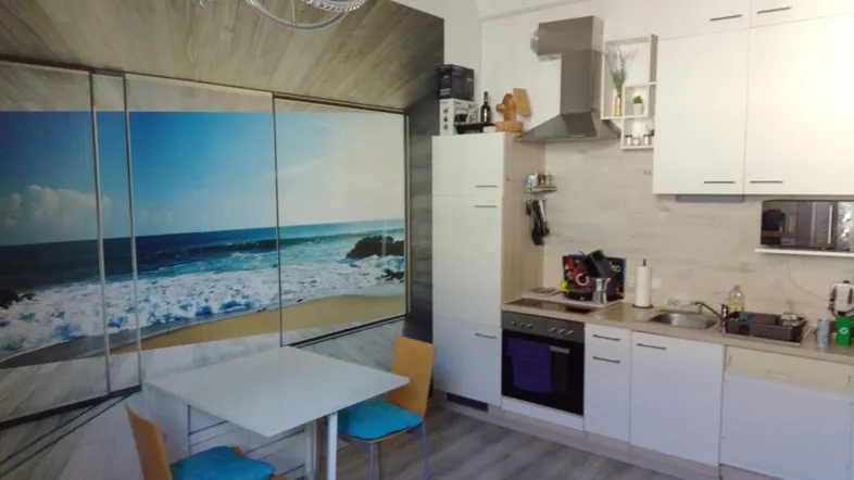 Moderne Küche mit weißen Schränken, Esstisch und einer großen Wandtapete mit Strandmotiv.