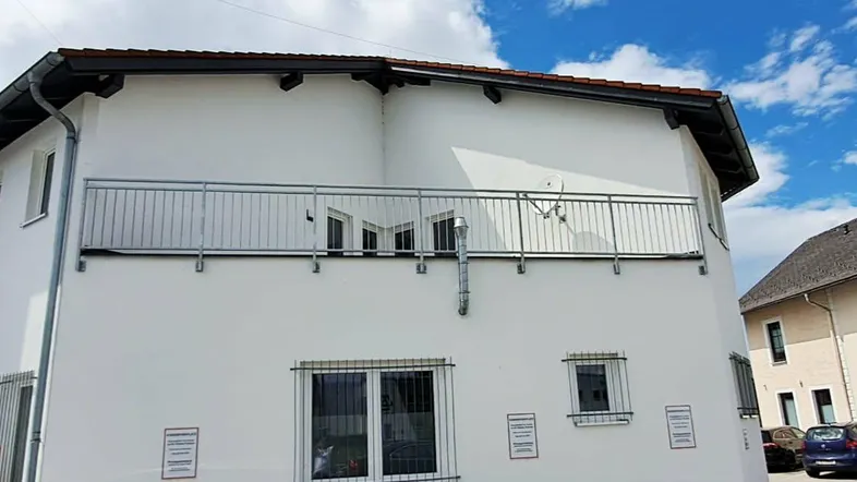 Außenansicht eines modernen Gebäudes mit weißer Fassade und einem Balkon mit Metallgeländer.