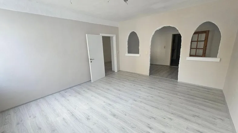 Helles, unmöbliertes Zimmer mit Laminatboden und dekorativen Rundbögen, frisch renoviert.