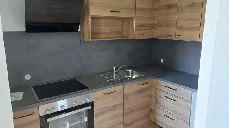 Moderne Einbauküche mit Holzoptikfronten, dunkler Arbeitsplatte und integrierten Geräten.