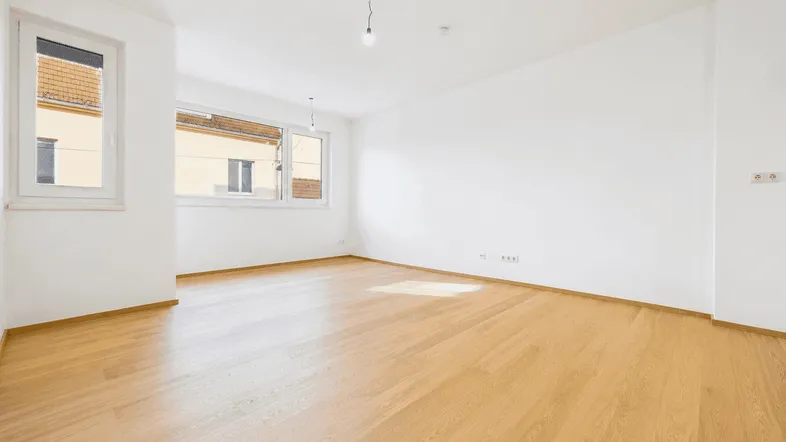 Helles, leeres Zimmer mit Parkettboden und großen Fenstern, bereit zur individuellen Gestaltung.