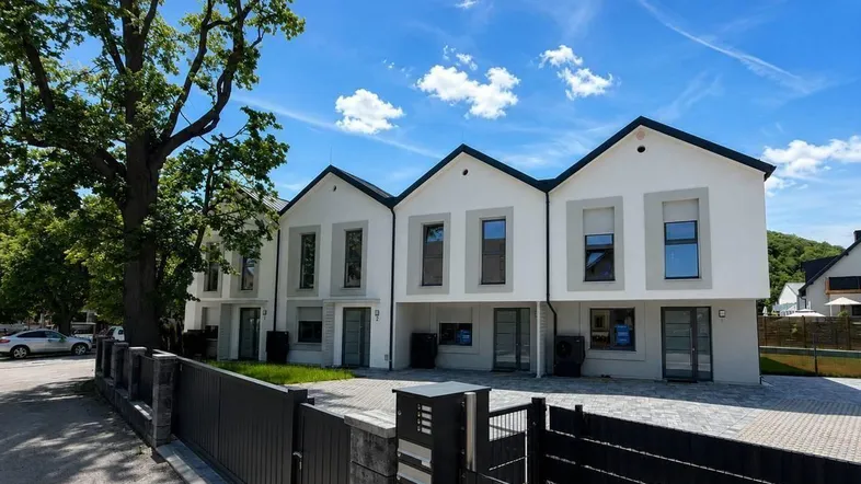 Moderne Reihenhäuser mit Satteldach und gepflastertem Vorplatz unter blauem Himmel.
