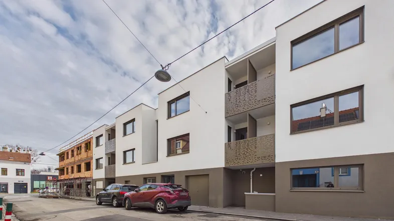 Moderne Wohngebäude mit weißer Fassade, Balkonen und Parkplätzen an der Straße.