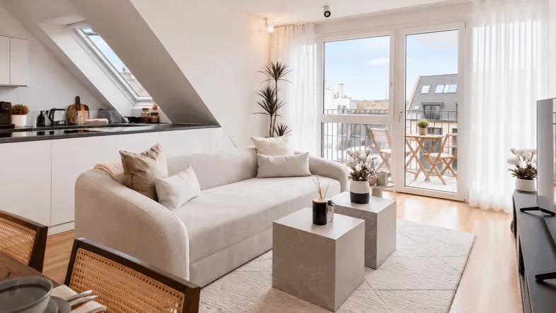 Helles Dachgeschoss-Apartment mit offenem Wohnbereich, moderner Küche und Zugang zum Balkon.