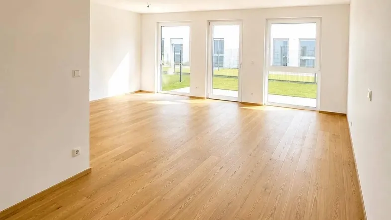 Helles, leeres Wohnzimmer mit Parkettboden und großen Fenstern zum Garten.