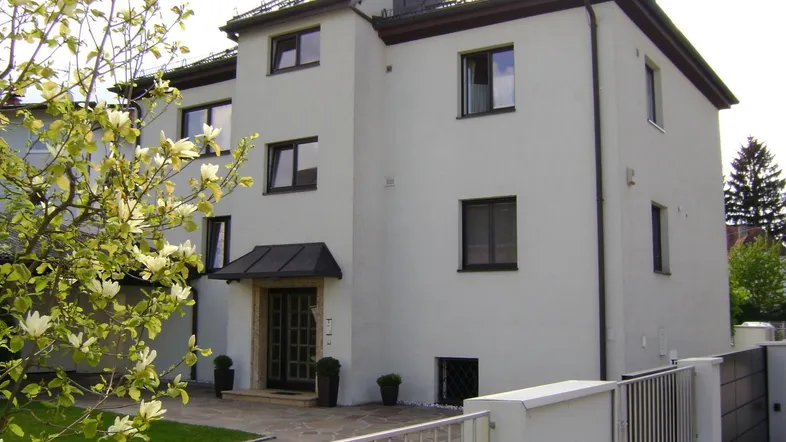 Modernes Wohnhaus mit weißer Fassade, dunklen Fenstern und gepflegtem Vorgarten.