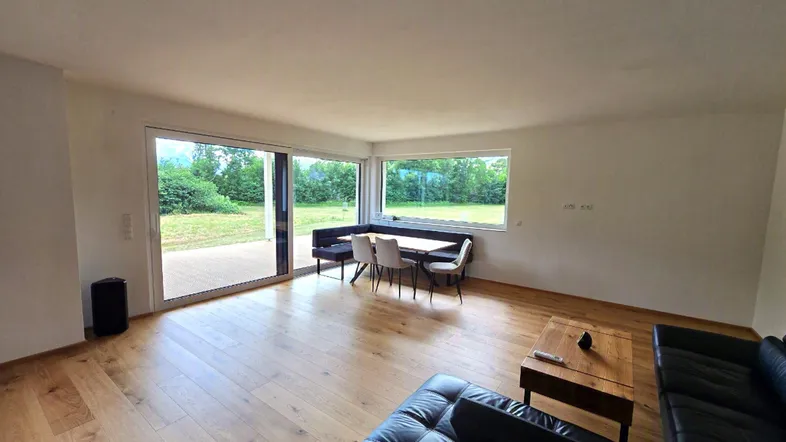 Heller, offener Wohn-Essbereich mit Holzboden, großen Fenstern und Zugang zur Terrasse mit Grünblick.
