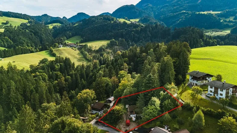 Luftaufnahme eines Grundstücks mit roter Umrandung, umgeben von Wäldern und Bergen.