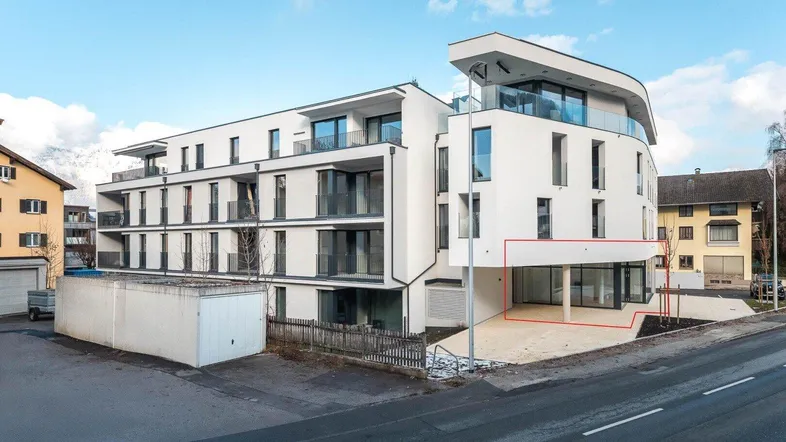Modernes Mehrfamilienhaus mit weißer Fassade, großen Balkonen und einer Gewerbefläche im Erdgeschoss.