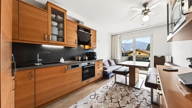 Moderne Holzküche mit Essbereich und Blick auf die Berge, ausgestattet mit Deckenventilator und Balkonzugang.