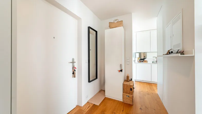 Heller Eingangsbereich mit Holzboden, einem schmalen Spiegel und Zugang zu weiteren Räumen.