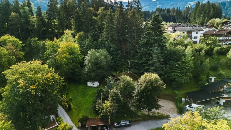 Panoramische Luftaufnahme eines Hauses im Grünen, umgeben von Wald und Bergen, mit einem Wohnwagen auf dem Grundstück.