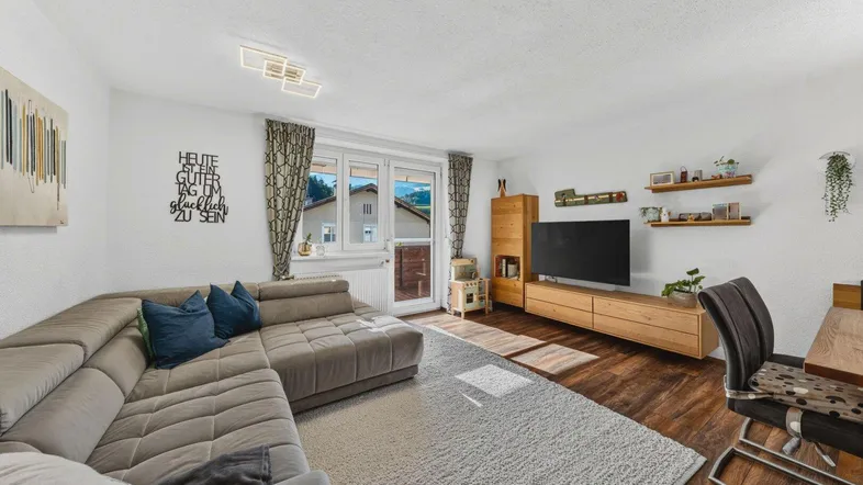Helles Wohnzimmer mit großem Ecksofa, Holzboden und Zugang zum Balkon mit Bergblick.