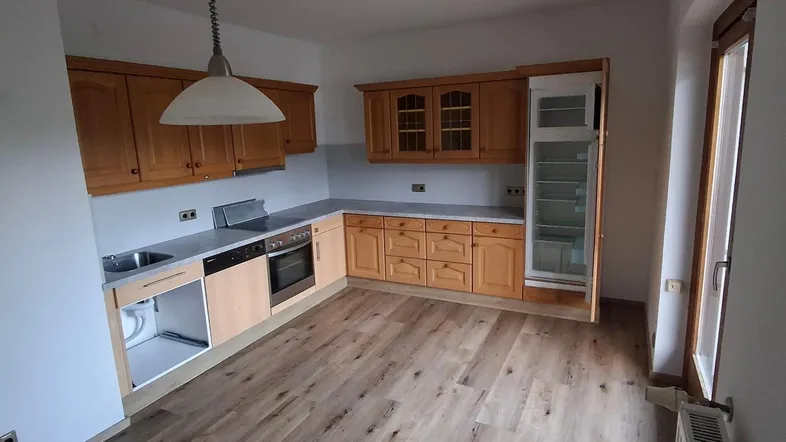 Geräumige Küche mit Holzschränken, Laminatboden und integriertem Kühlschrank, bereit für die individuelle Gestaltung.