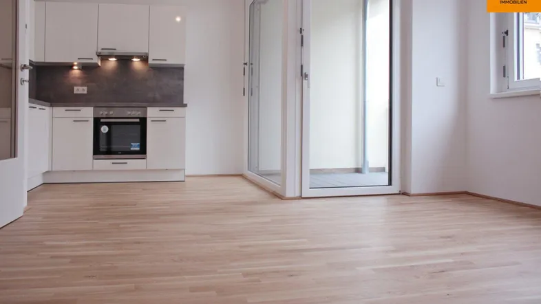 Helle Wohnküche mit moderner Einbauküche, Parkettboden und Zugang zum Balkon.