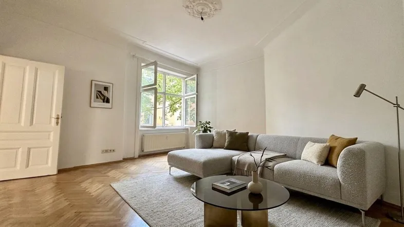 Helles Wohnzimmer mit Fischgrätparkett, Stuckdecke und modernem Sofa.