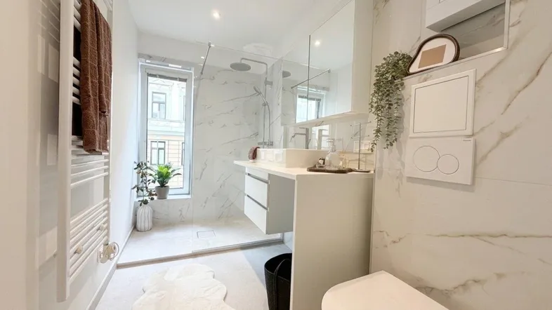 Modernes Badezimmer mit großformatigen Marmorfliesen, ebenerdiger Dusche und elegantem Waschtisch.