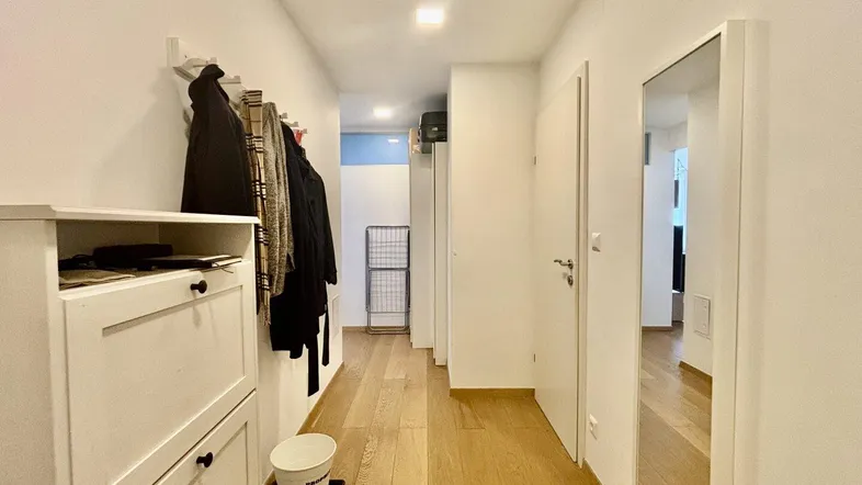 Heller Flur mit Holzfußboden, Schuhschrank und großem Spiegel.