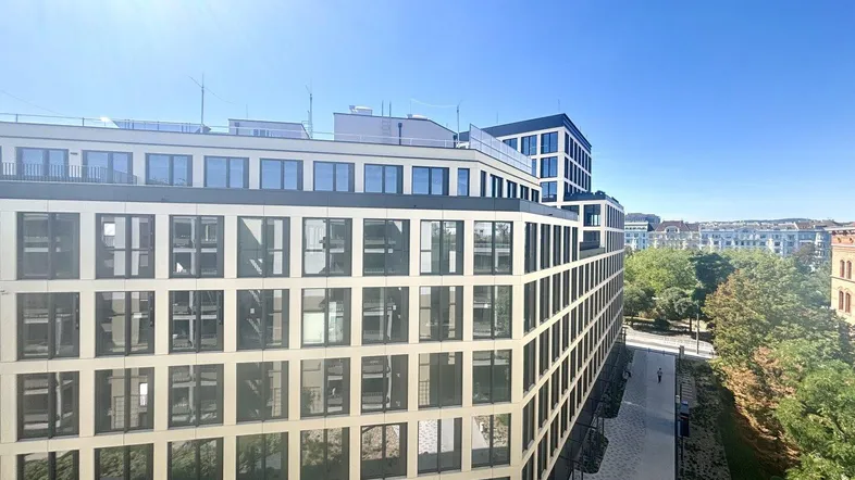 Moderne Wohngebäude mit vielen Fenstern und sonnigem Himmel, umgeben von Grünflächen.