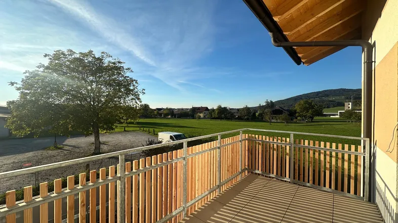 Geräumiger Balkon mit Holzelementen und weitem Blick über grüne Felder und die Landschaft.