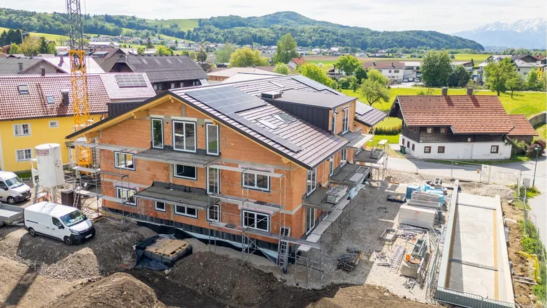 Luftaufnahme eines im Bau befindlichen Gebäudes mit Solarpaneelen auf dem Dach und Bergblick.
