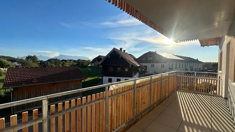 Sonniger Balkon mit Holzelementen und weitem Blick über die ländliche Umgebung.