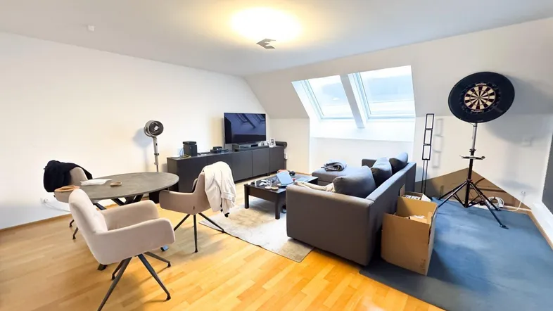 Helles Dachgeschoss-Wohnzimmer mit Holzboden, Dachfenstern und einem gemütlichen Sofa.