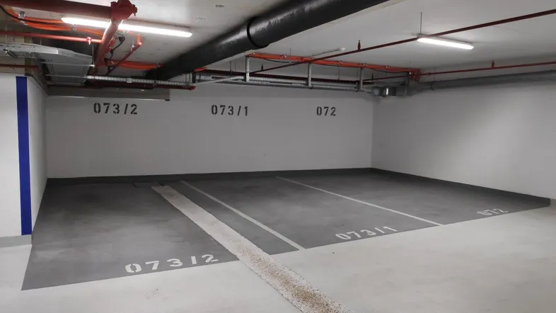 Tiefgaragenstellplatz mit Betonboden und sichtbaren Installationen an der Decke in einem Neubau.