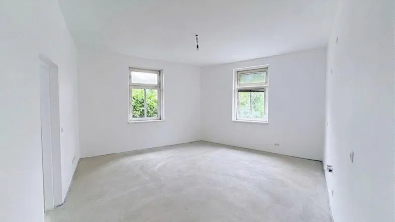 Helles, unmöbliertes Zimmer mit weiß gestrichenen Wänden und Estrichboden, bereit für den Ausbau.