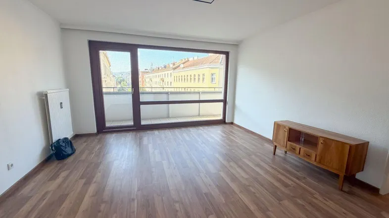 Helles Wohnzimmer mit Laminatboden und Zugang zu einem Balkon mit Stadtblick.