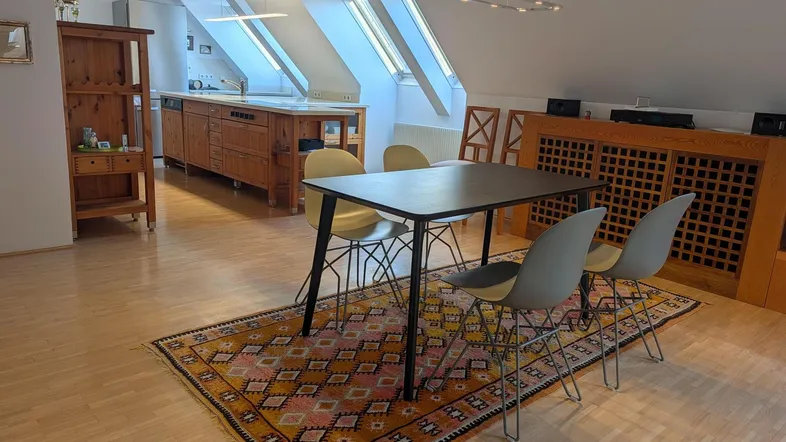 Geräumiger offener Wohn- und Essbereich mit Holzküche, Esstisch und Dachfenstern in einer Dachgeschosswohnung.