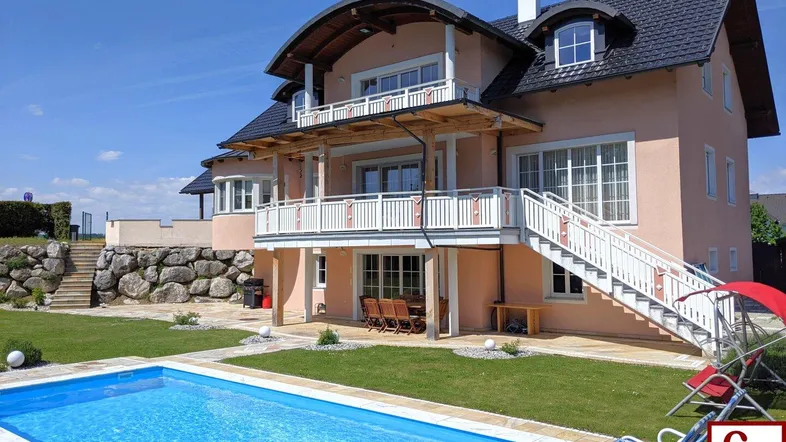 Großzügiges Einfamilienhaus mit weitläufigem Garten, privatem Pool und mehreren Balkonen unter blauem Himmel.