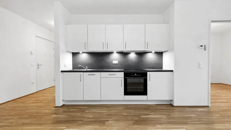 Moderne Einbauküche mit weißen Schränken, dunkler Arbeitsplatte und integriertem Backofen.