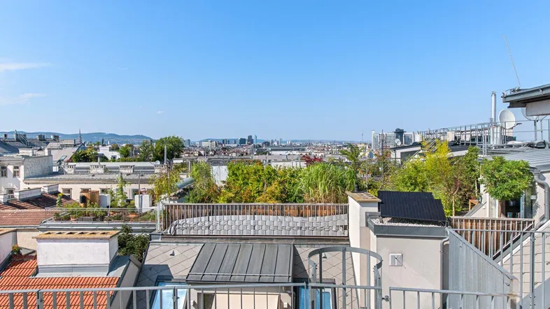 Panoramablick über die Stadt Wien von einer Dachterrasse mit umliegenden Gebäuden und viel Grün.