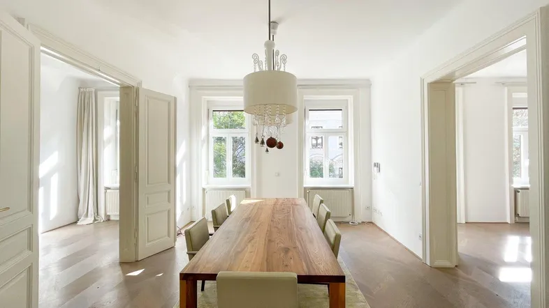 Helles Esszimmer mit Holztisch, modernen Stühlen und Fischgrätparkett, verbunden mit weiteren Räumen.