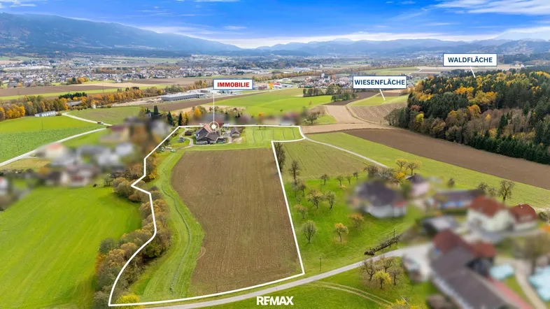 Luftaufnahme des Anwesens mit umrandetem Grundstück, umgeben von Wiesen, Wald und Bergen in der Ferne.