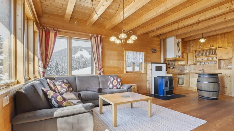 Gemütlicher Wohn- und Essbereich mit viel Holz, Kaminofen und weitem Blick auf die verschneite Berglandschaft.