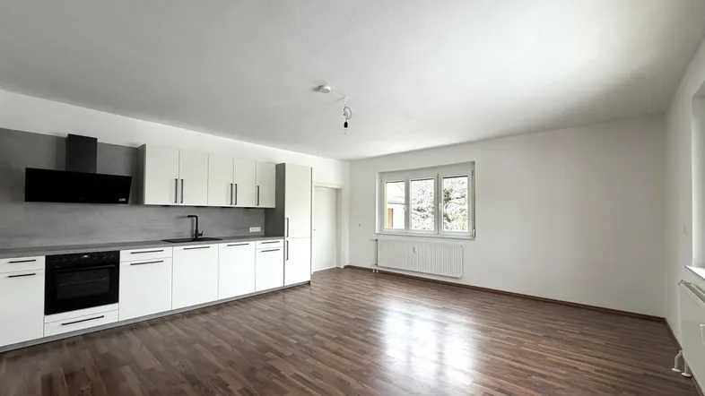 Geräumiger offener Wohn-Essbereich mit moderner Einbauküche und dunklem Parkettboden.