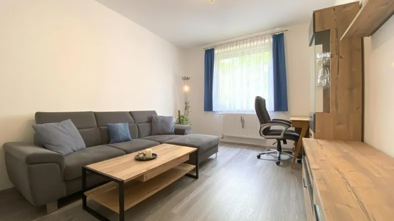 Gemütliches Wohnzimmer mit grauem Ecksofa, Couchtisch und integriertem Arbeitsbereich.