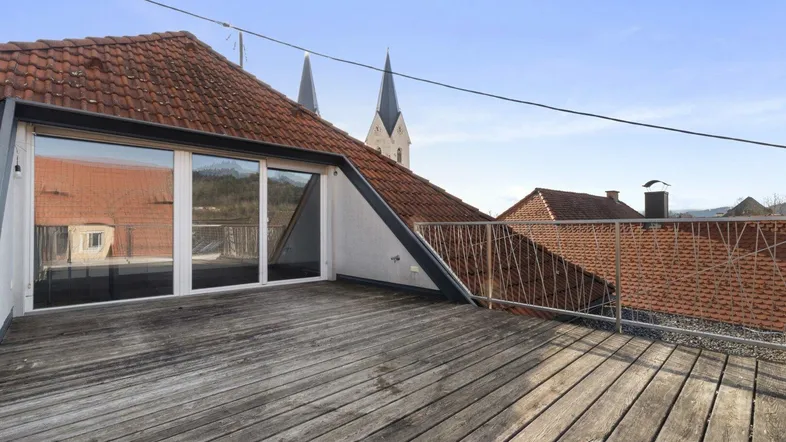 Geräumige Dachterrasse mit Holzboden und weitem Blick über die Dächer und Kirchtürme der Stadt.