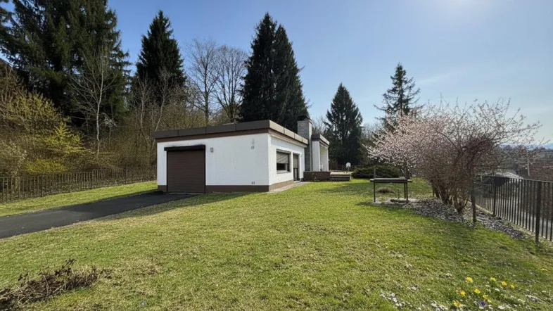 Modernes Einfamilienhaus mit Flachdach, Garage und weitläufigem Gartenbereich unter strahlendem Himmel.